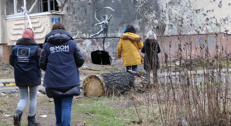 Сотрудники МОМ проходят мимо разрушенного войной здания с граффити балерины в Киевской области.